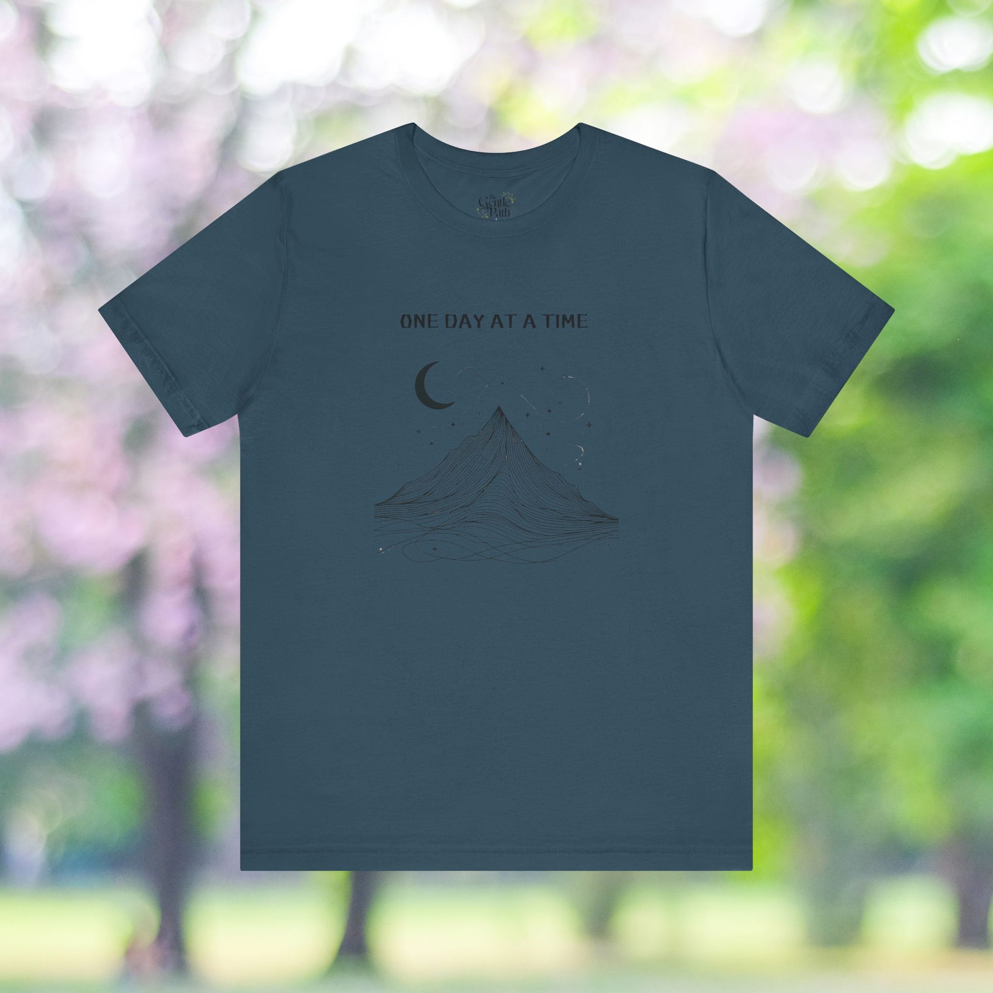 Teal T-shirt with minimalist mountain, moon, and 'One Day at a Time' design.